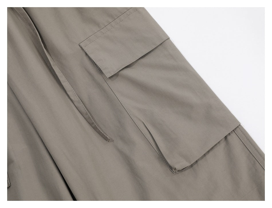 Close-up of a taupe cargo trouser flap pocket and a dangling waist drawstring.
