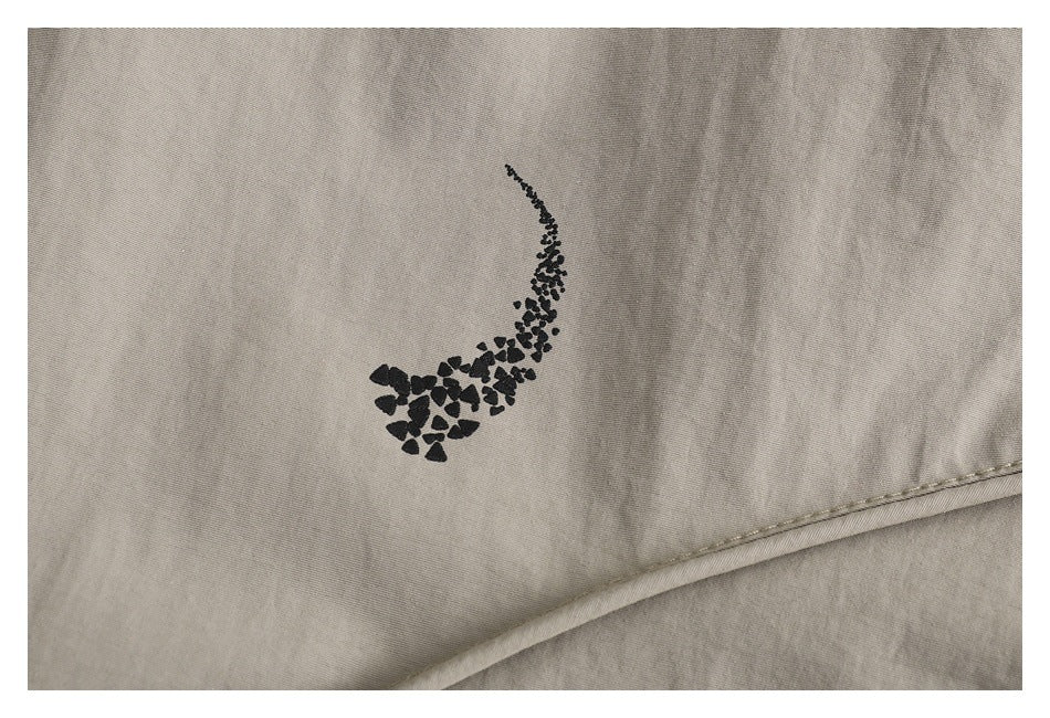 Close-up of a black abstract motif printed on taupe jacket fabric above a diagonal seam.