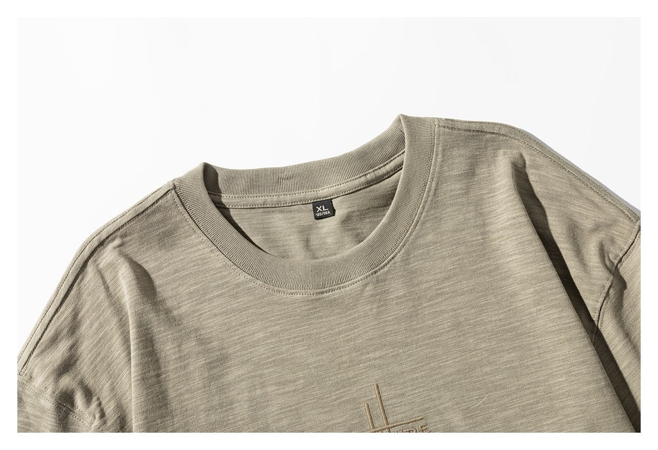 Close-up of the khaki shirt's crew neckline, XL neck label, and partially visible tonal chest embroidery.