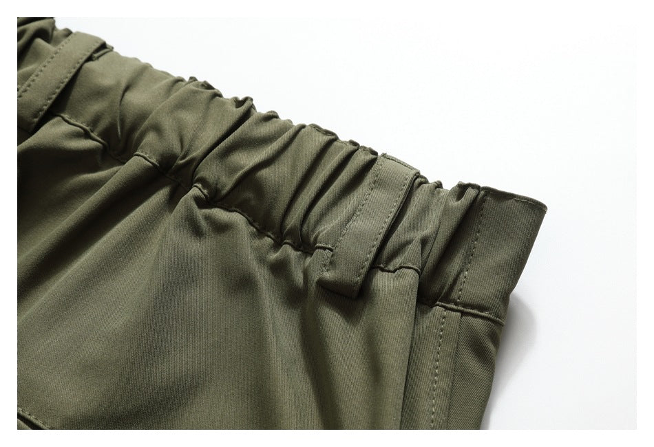 Close-up of olive-green pants showing a gathered elastic waistband, belt loop, and side seam.