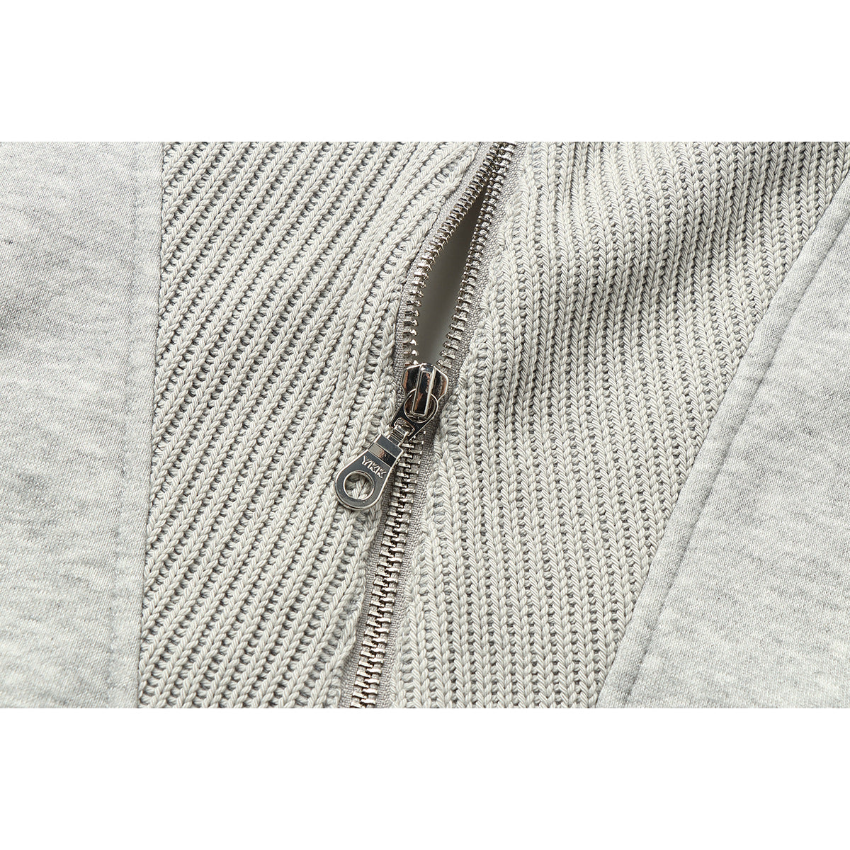 Close-up of the metal zipper and textured knit panels on a light gray jacket.