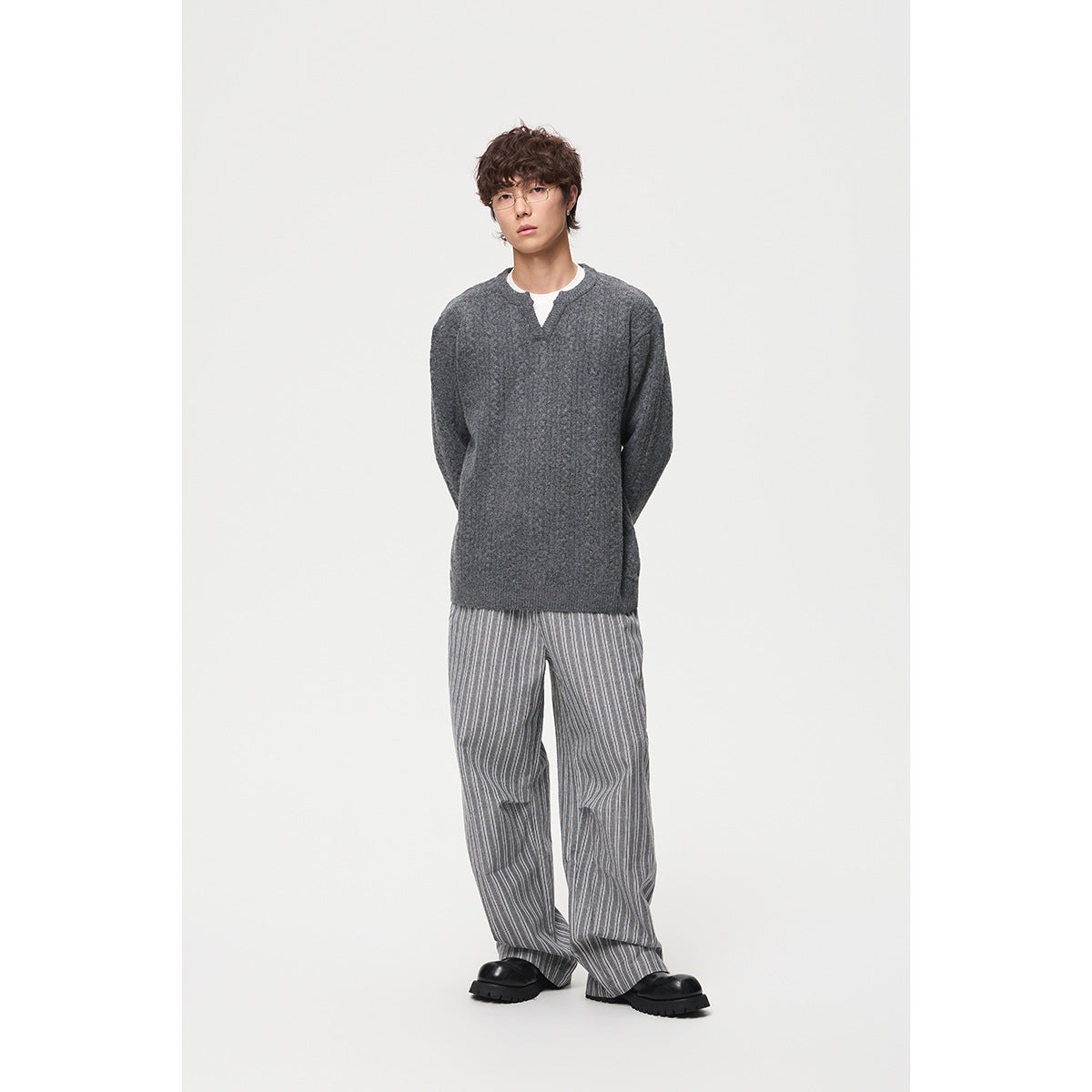 Full-length model wearing a charcoal gray split-neck sweater with wide gray striped trousers and black shoes.