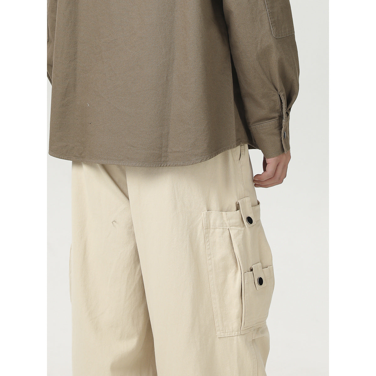 Close-up of a taupe shirt hem and cuff above cream cargo pants with buttoned pockets.