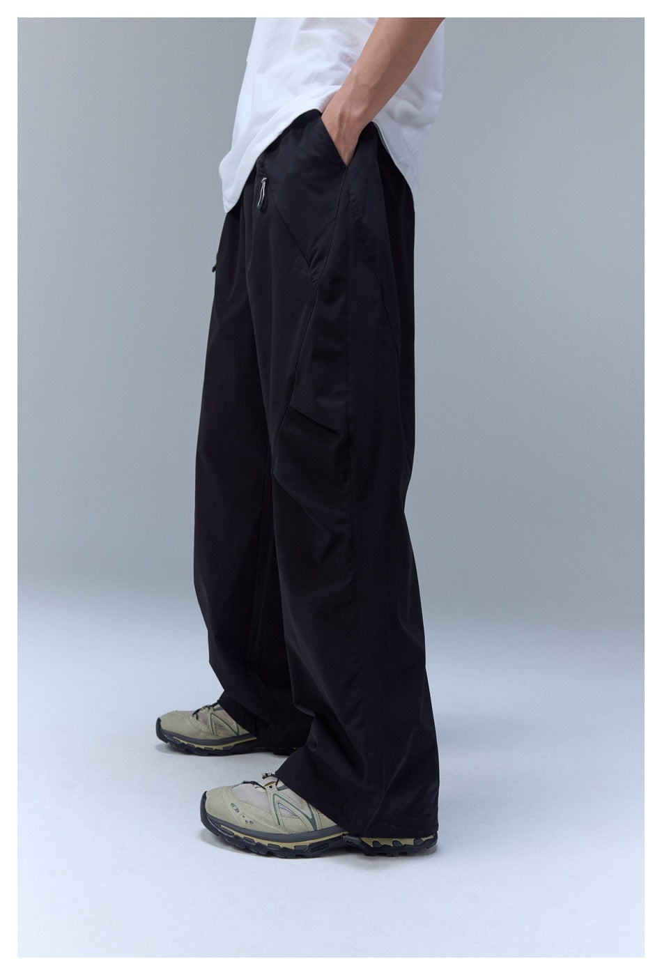 Side view of a model wearing loose black wide-leg pants with an elastic cuff and sneakers.