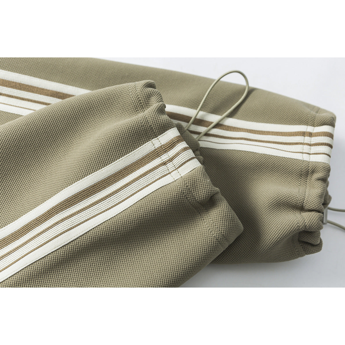 Close-up of olive joggers with cream and brown side stripes, a gathered cuff and drawcord.