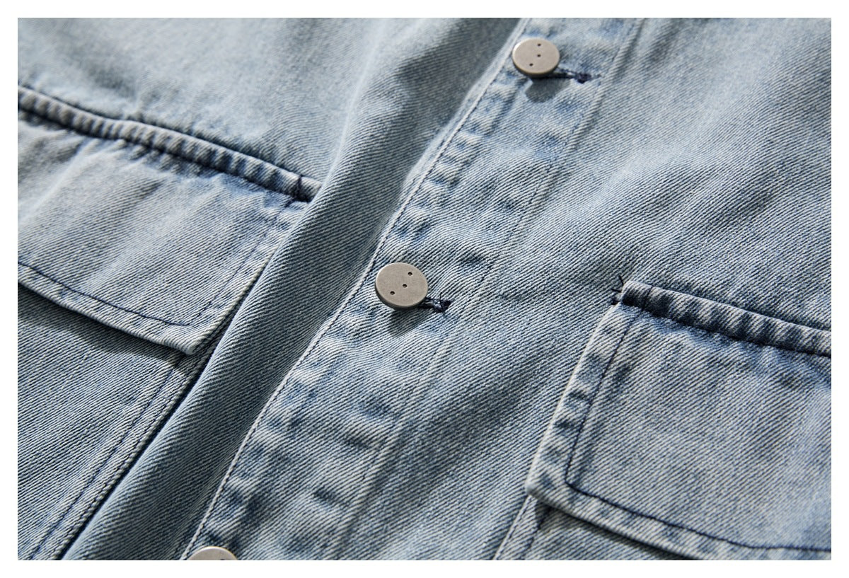 Close-up of a light blue washed denim jacket showing its button placket and two flap chest pockets.