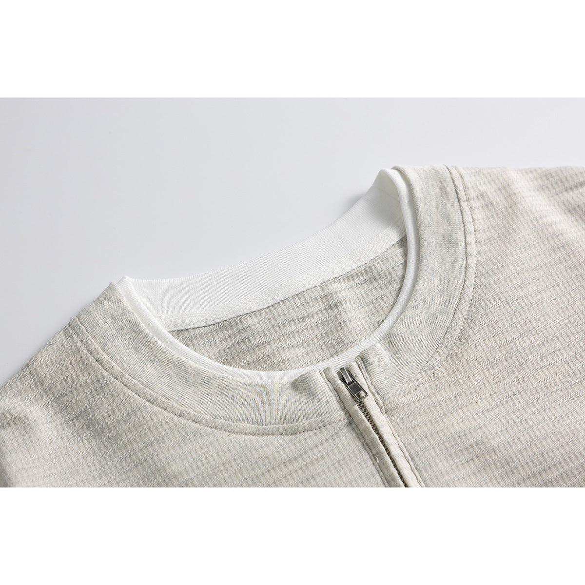 Close-up of a light heather short-sleeve shirt neckline and closed silver quarter-zip.