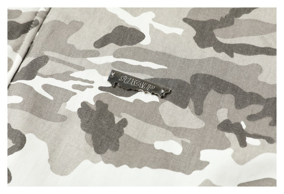 Close-up of a small silver-colored metal plaque on the jacket's gray camouflage fabric.