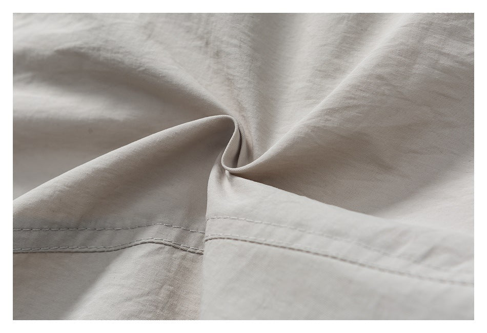 Close-up of light gray-beige pant fabric gathered into a twist, with a stitched seam visible.