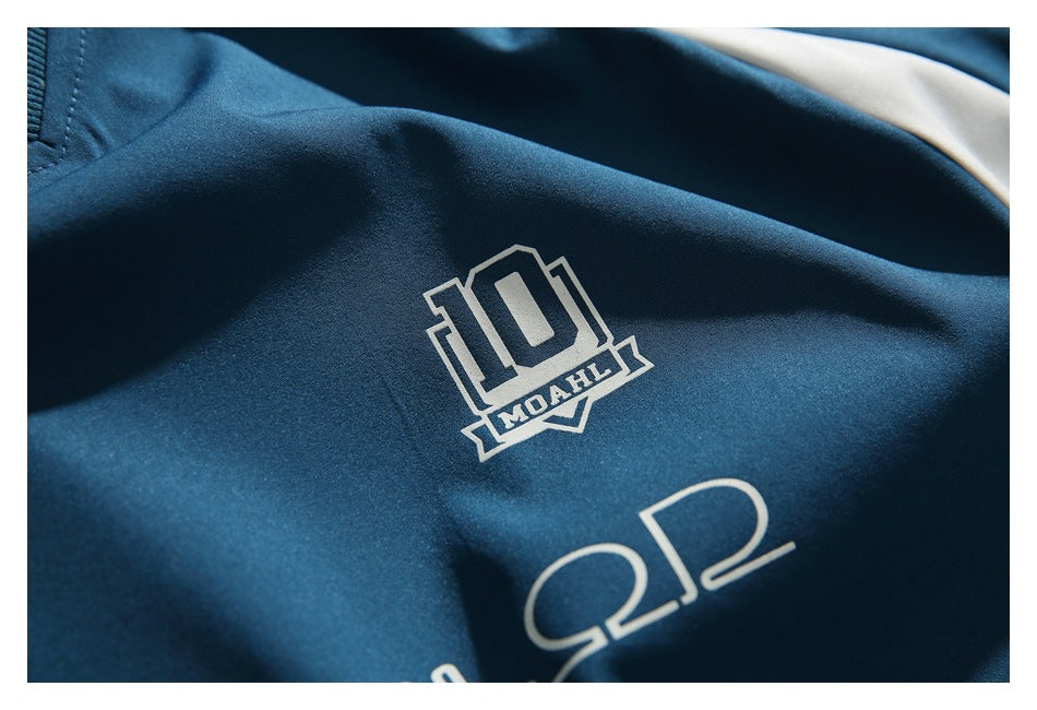 Close-up of a teal garment with a small cream emblem and larger outlined lettering printed on the fabric.
