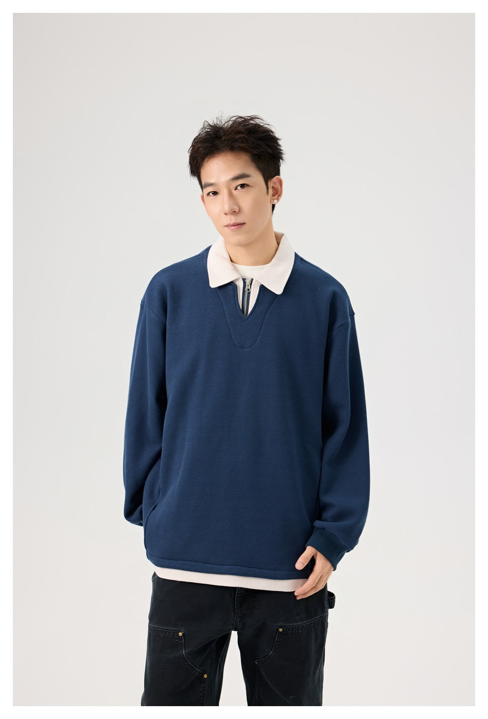 Model wearing a navy pullover with a cream collar and short zip neckline, shown from the front.