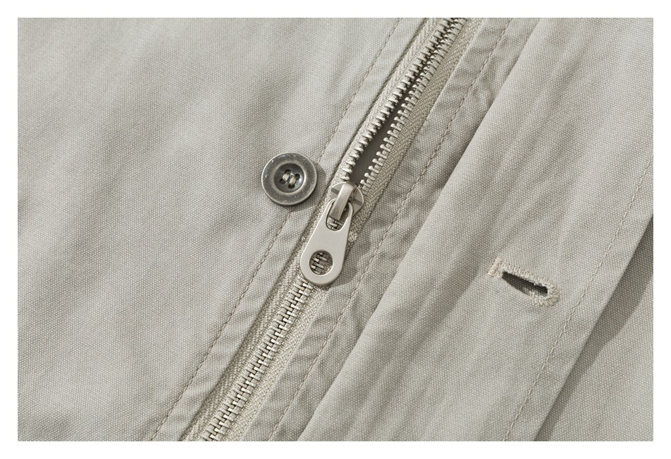 Close-up of a light khaki jacket front showing a metal zipper, button, and buttonhole.
