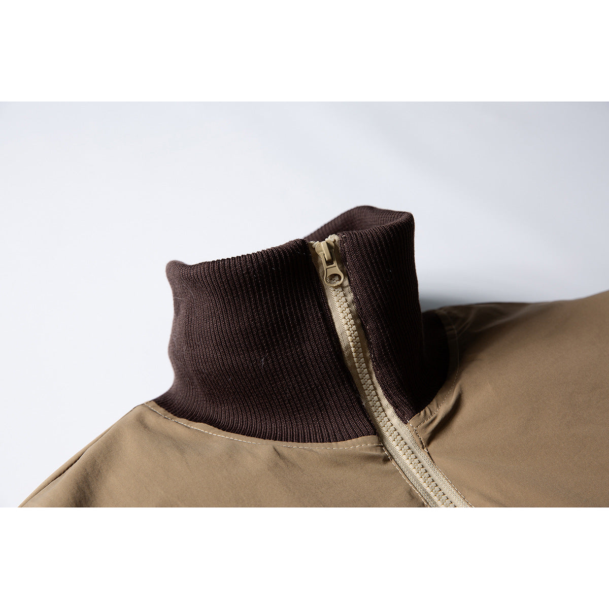Close-up of a tan jacket’s dark brown ribbed stand collar and light-colored zipper.
