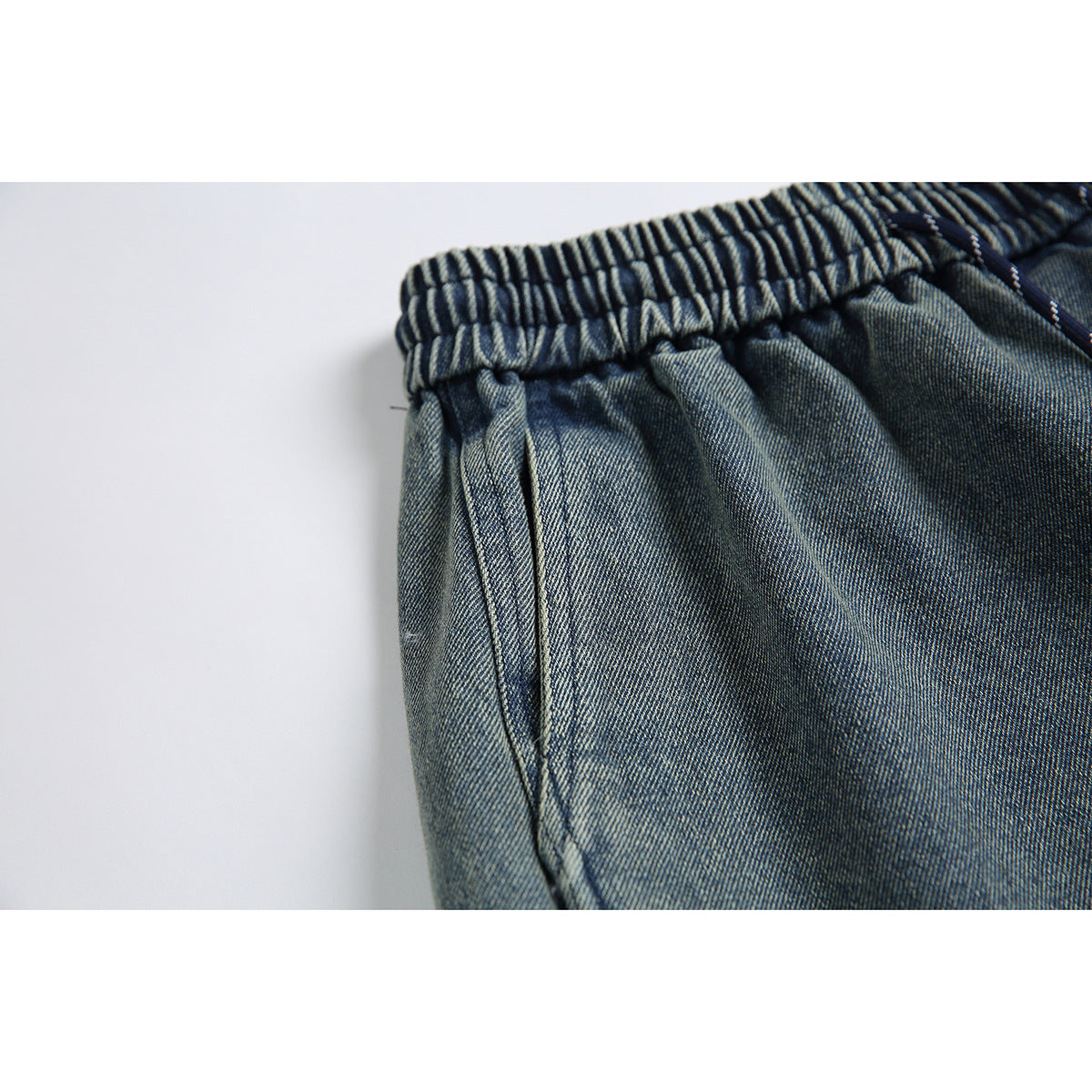 Close-up of the gathered elastic waistband and side pocket on blue-gray denim shorts.
