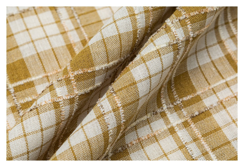 Close-up of mustard and cream plaid fabric folds, showing the woven texture and frayed seam edges.