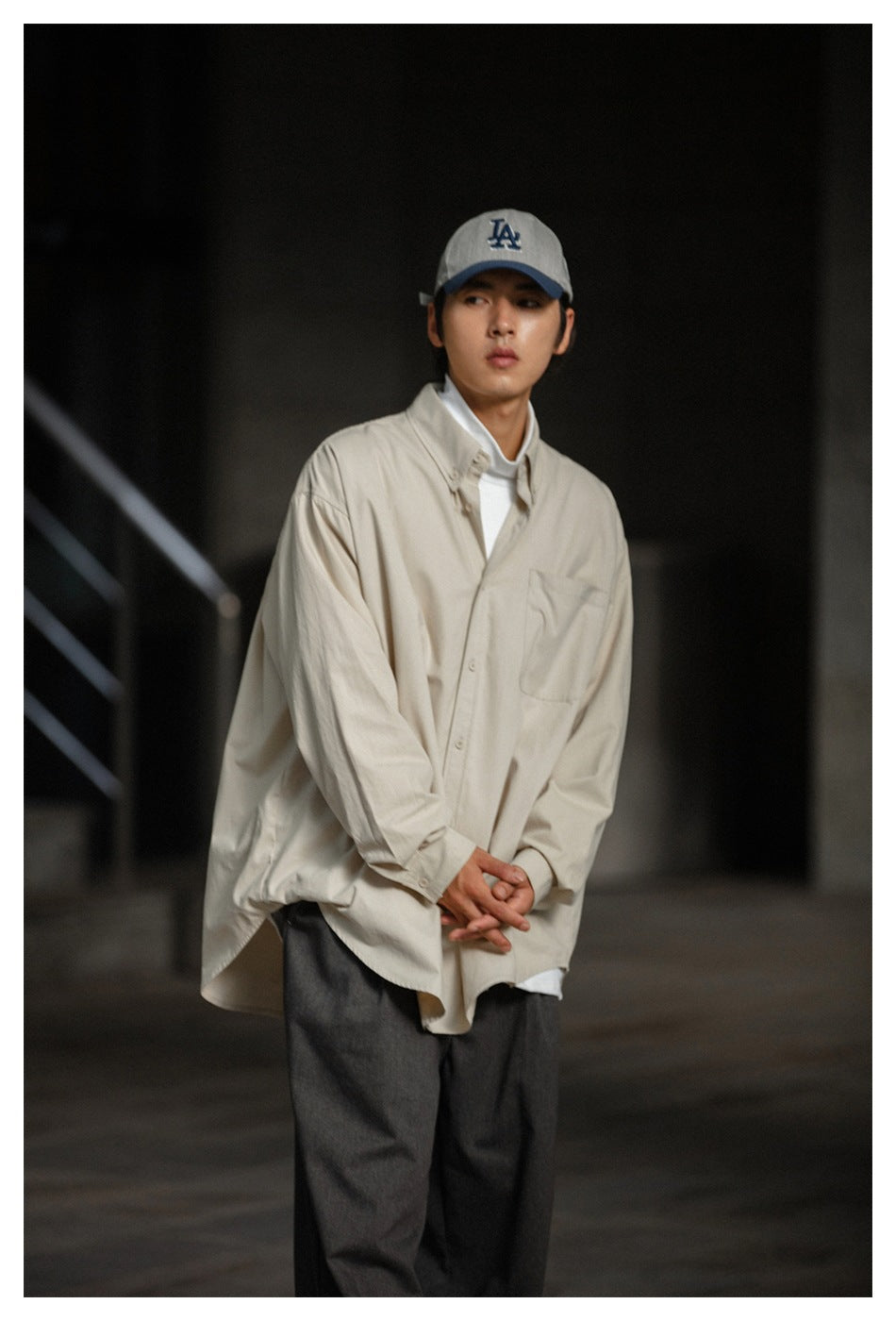 Model wearing an oversized cream button-up shirt over a white top with dark trousers.