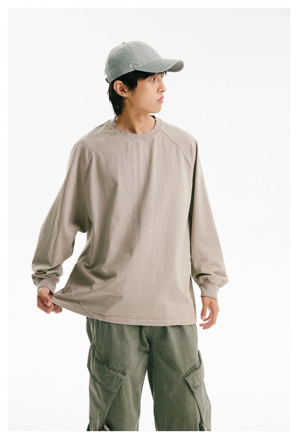 Model wearing an oversized taupe long-sleeve raglan shirt with a crew neck, shown from the front with a slight side view.