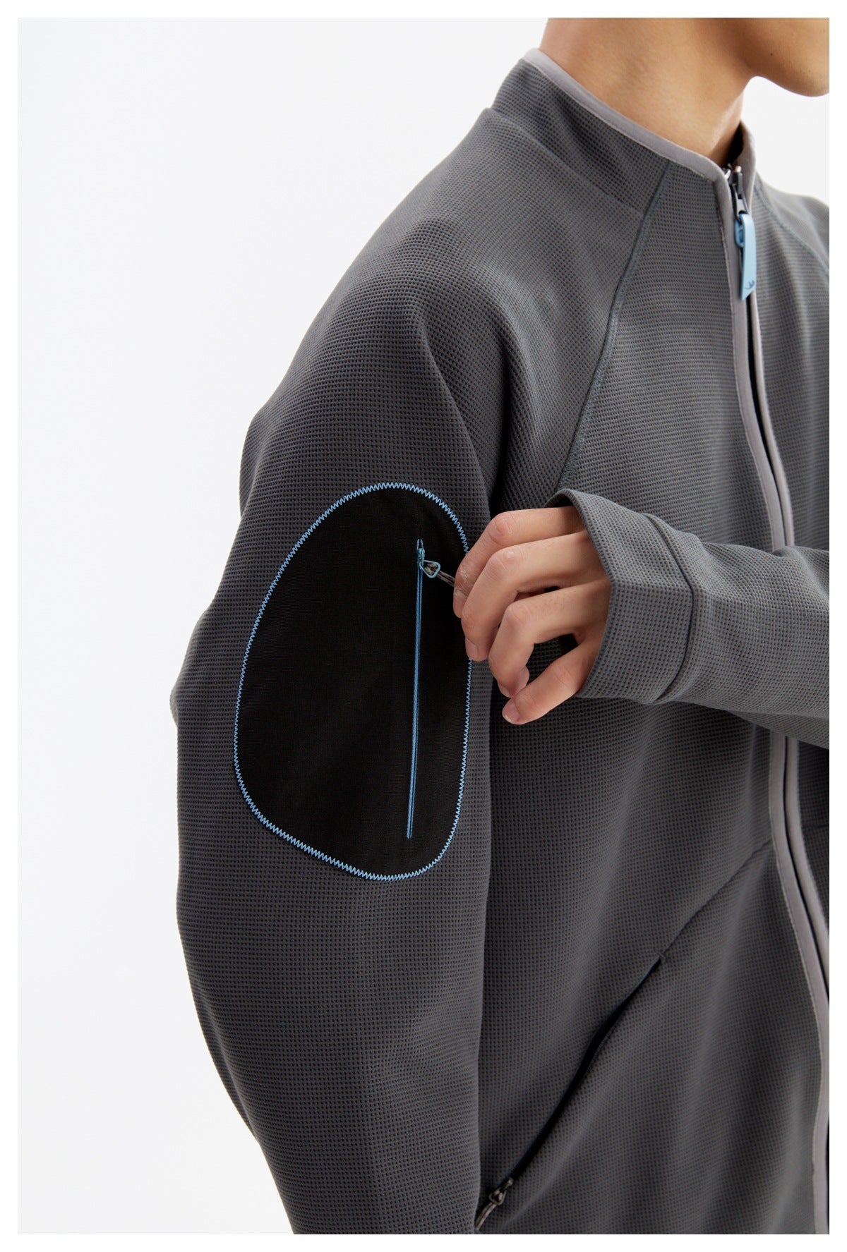 Close-up of the jacket's black upper-sleeve zip pocket with blue stitching and a gray textured surface.