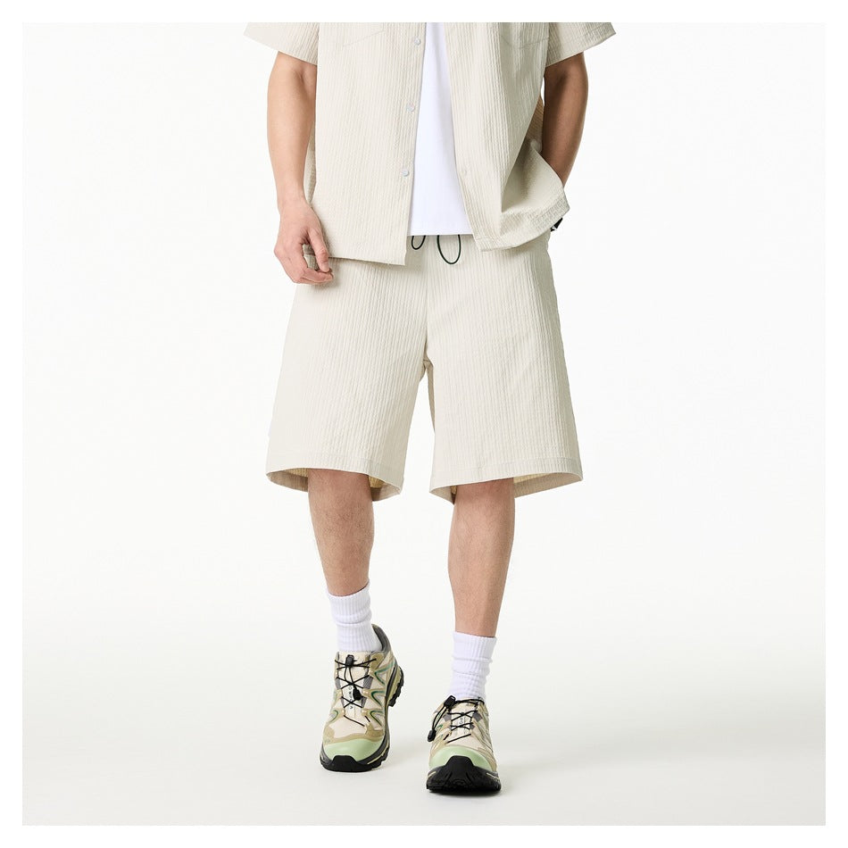 Cropped front view of a model wearing ivory drawstring shorts with a matching short-sleeve shirt and white tee.