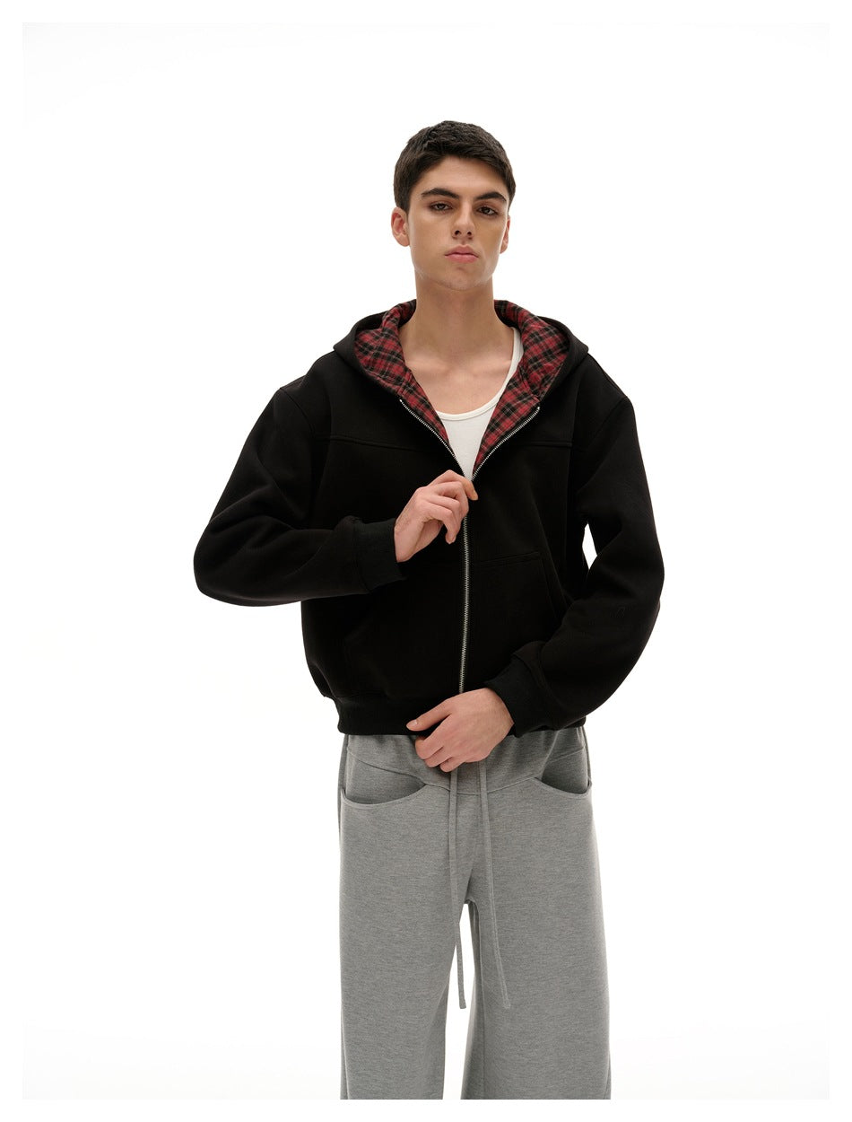 Closer view of a model wearing a black zip-up hoodie with red plaid hood lining and loose gray pants.