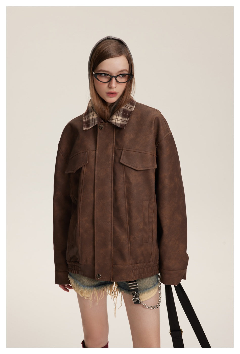 Model wearing an oversized brown jacket with a brown plaid collar, flap chest pockets, and an elasticated hem.