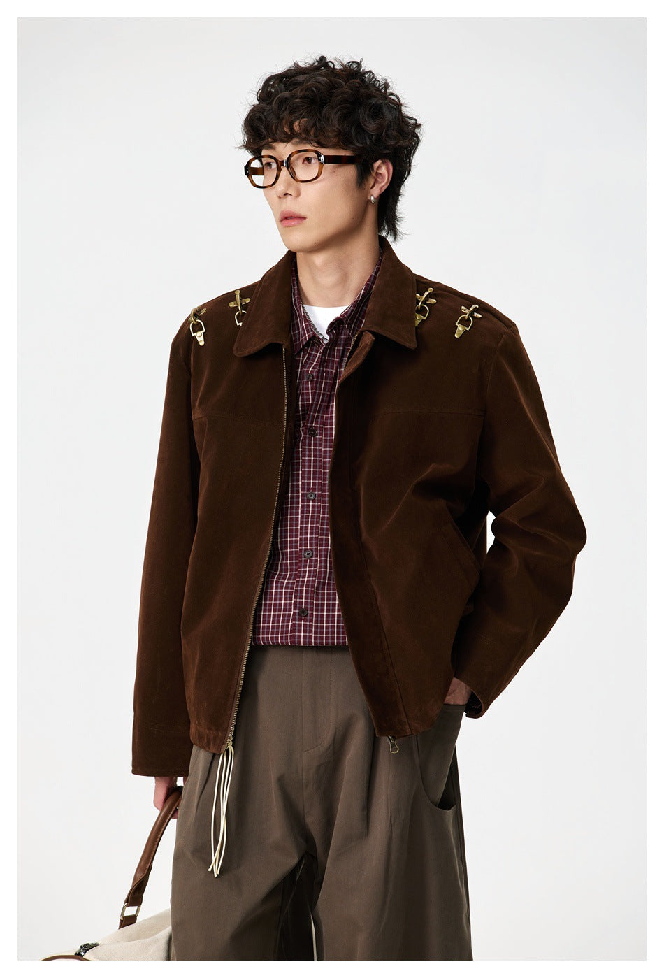 Model wearing a dark brown jacket with brass shoulder hardware over a burgundy plaid shirt.
