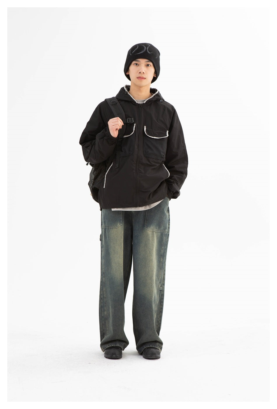 Full-length front view of a man in a black hooded jacket with white-trimmed pockets and loose jeans.