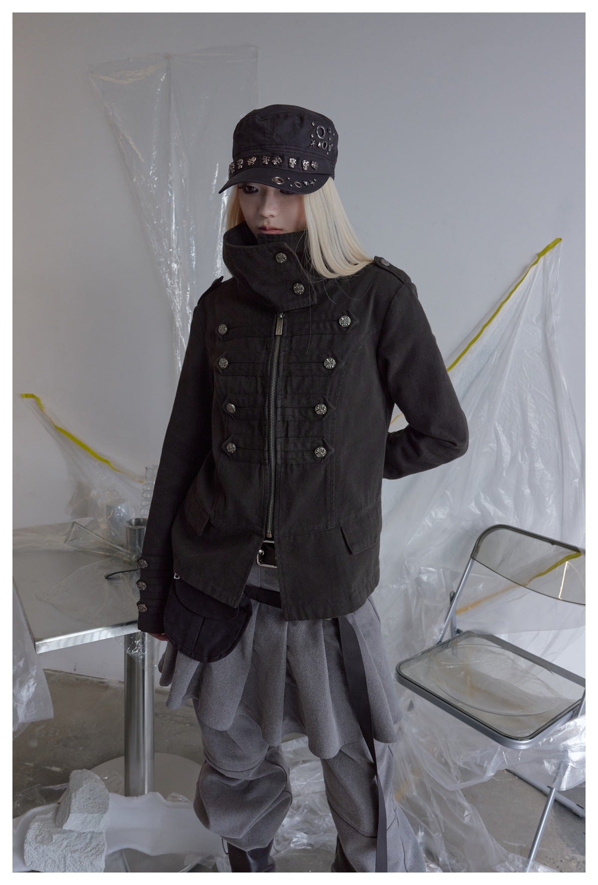 A model wears a black zip-front jacket with a high collar and decorative buttons over gray layered clothing.