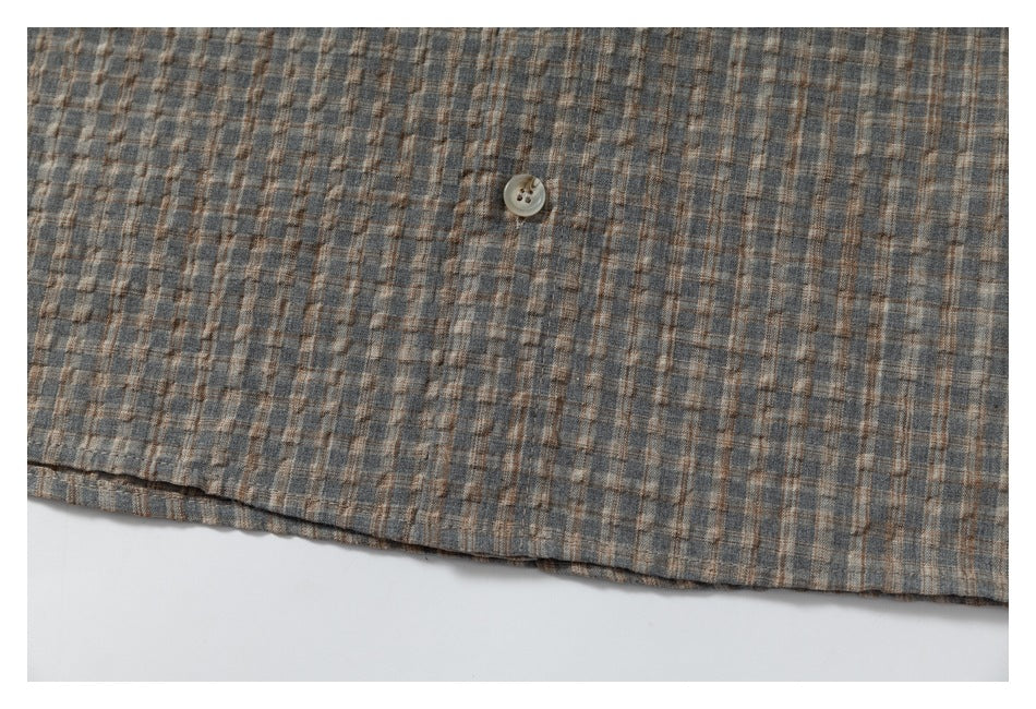 Close-up of the lower edge and button of a gray-brown plaid garment.