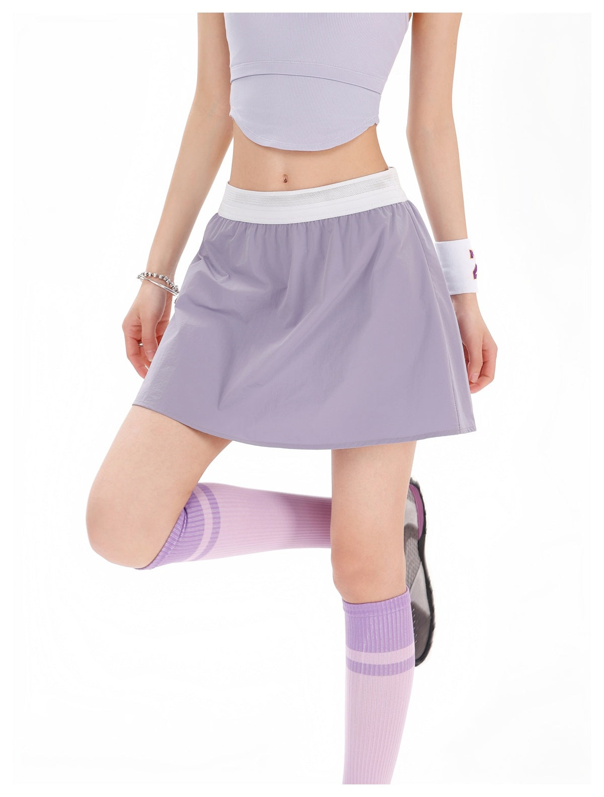 Model wearing a lavender tennis skirt with a white waistband, lilac crop top and striped knee socks, front view.