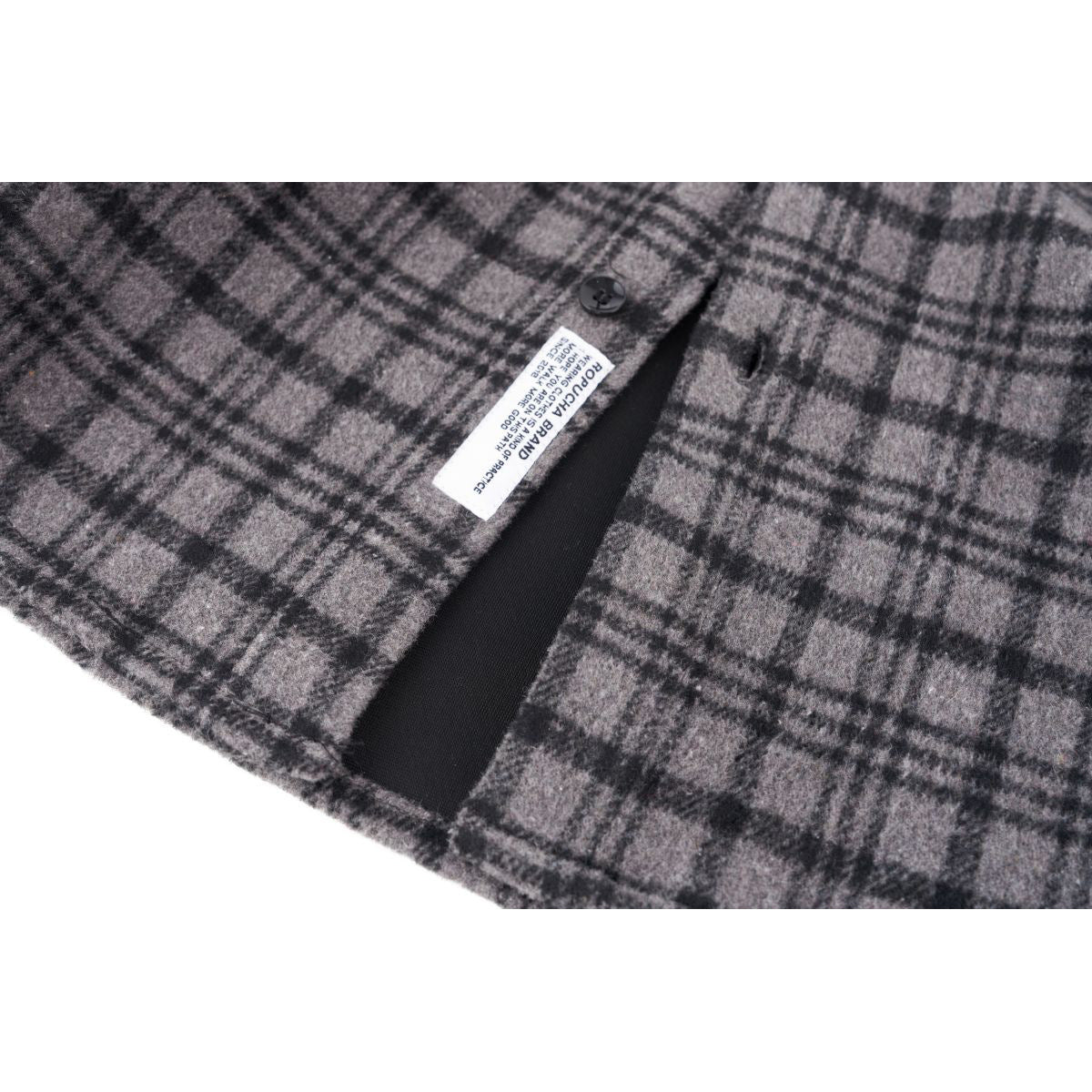 Close-up of gray and black plaid shirt fabric, a black button, and a sewn-in care label.