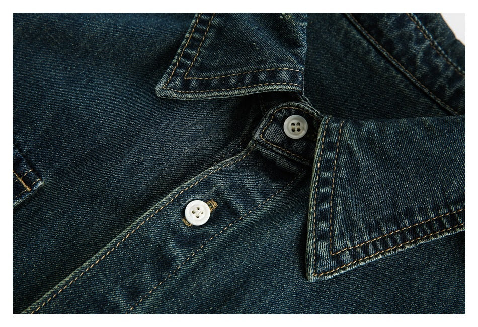 Close-up of the dark indigo denim shirt placket, collar edge, white buttons and tan stitching.