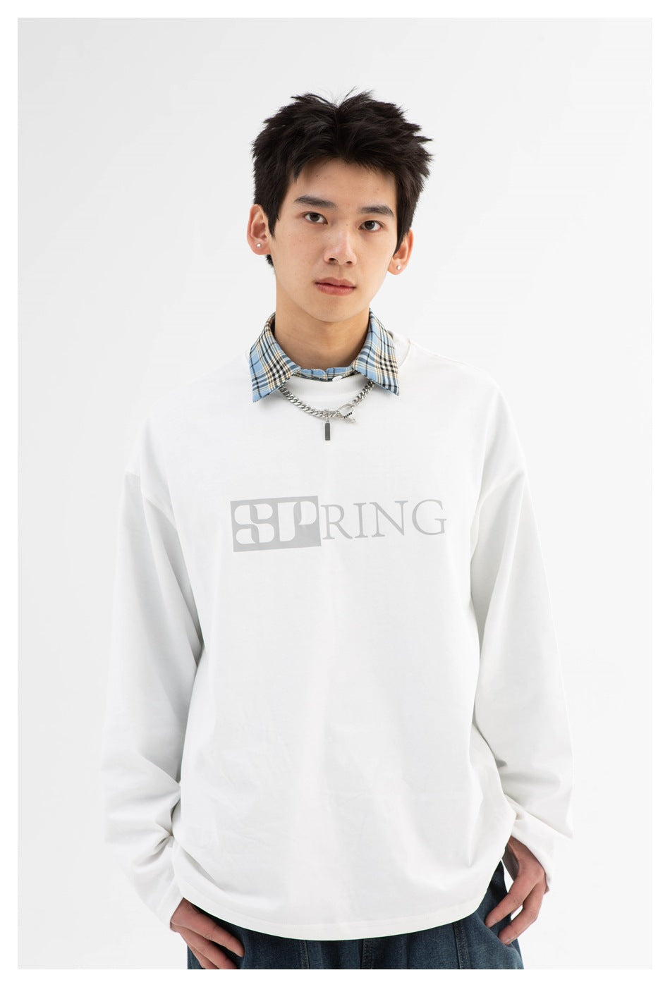 Close view of a model wearing a white long-sleeve shirt with a large gray SPRING chest graphic and blue plaid collar.