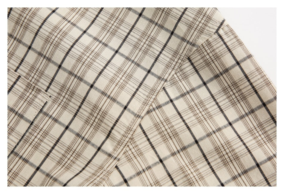 Close-up of beige fabric with intersecting black and brown plaid lines and a stitched seam.