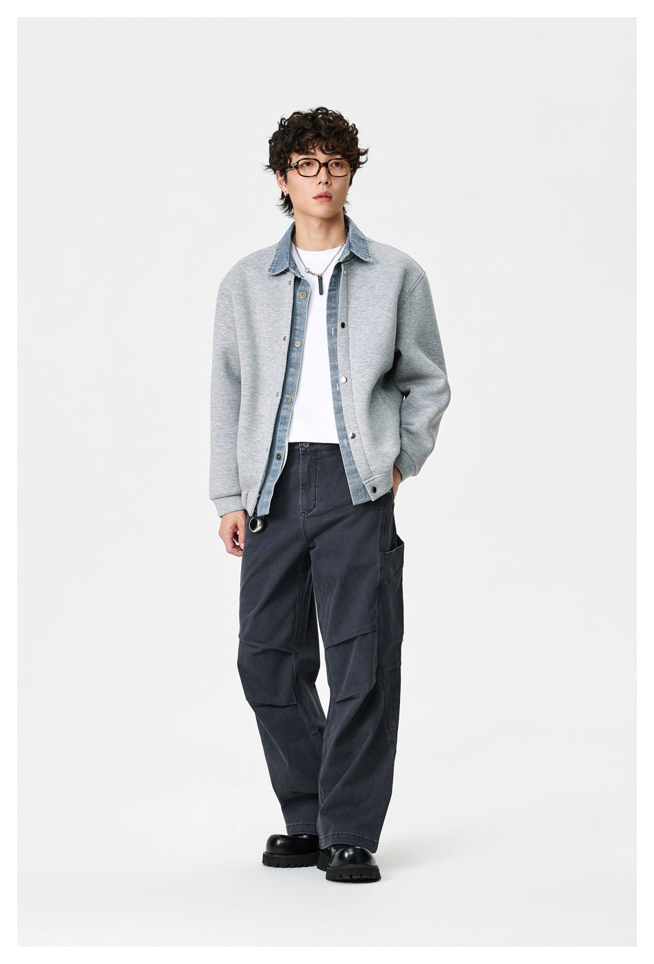 Full-length model wearing a light gray jacket with blue denim trim, white tee, dark cargo pants, and black shoes.
