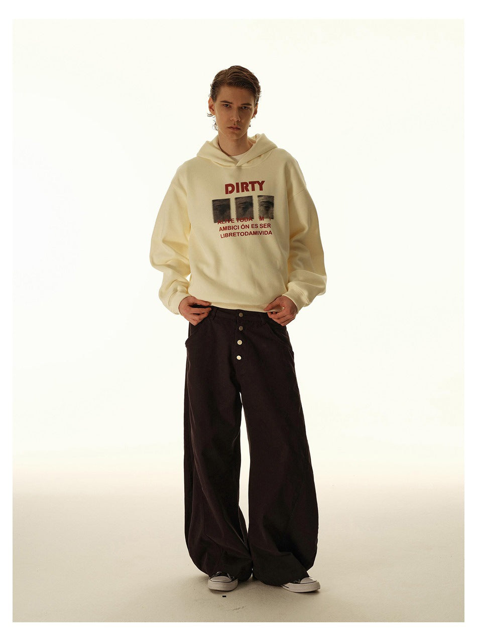 Front view of a model in a cream graphic hoodie and wide black trousers, standing against a light studio backdrop.