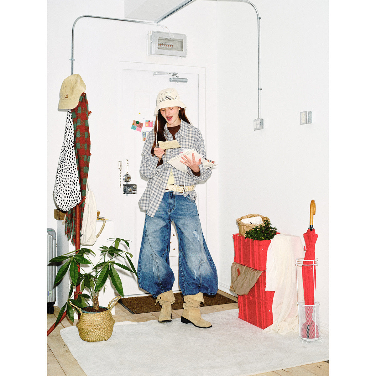 Full-length model wearing a gray-blue plaid button-down shirt, oversized blue jeans, cream crochet hat and tan boots.
