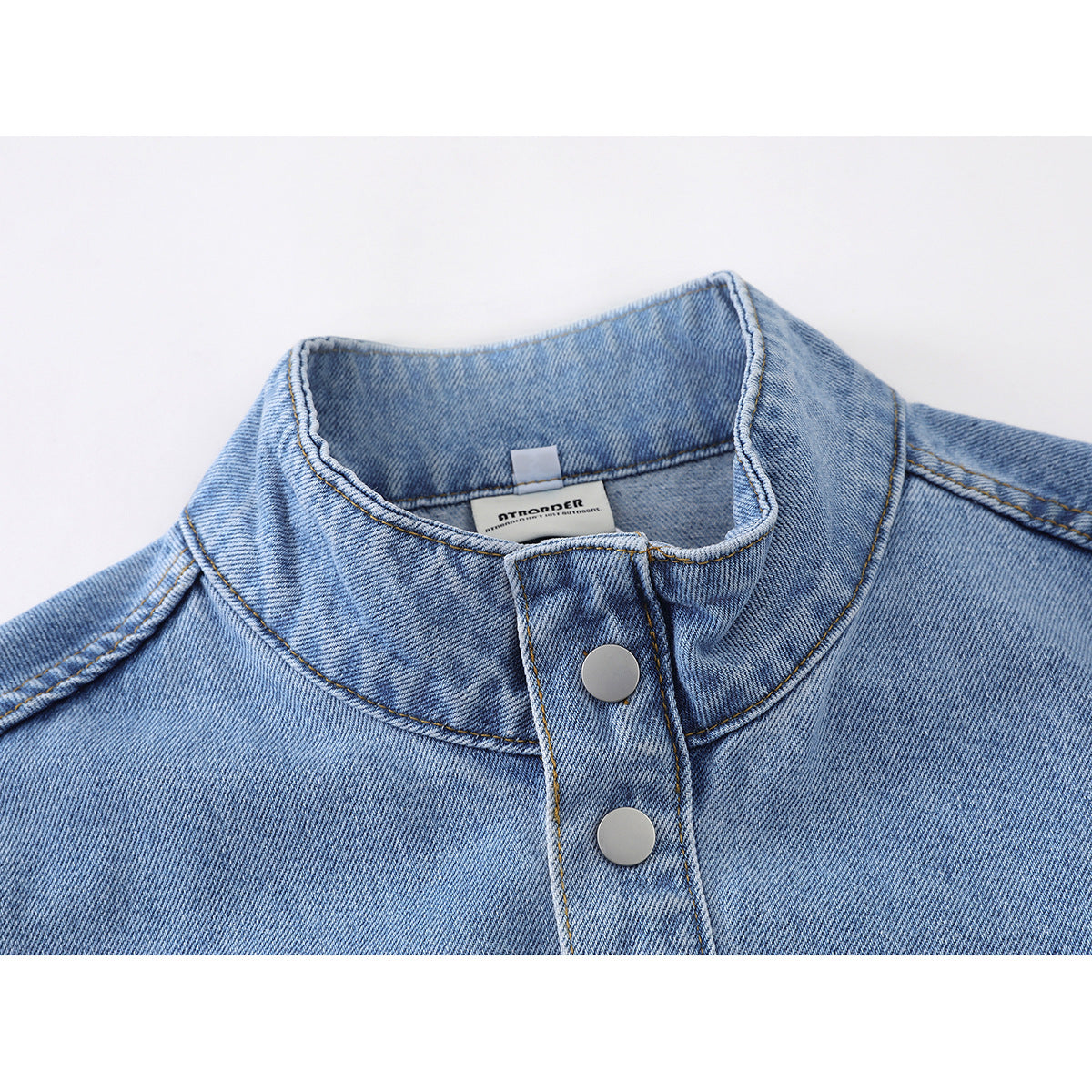 Close-up of a light blue denim jacket’s stand collar and silver snap-button placket.
