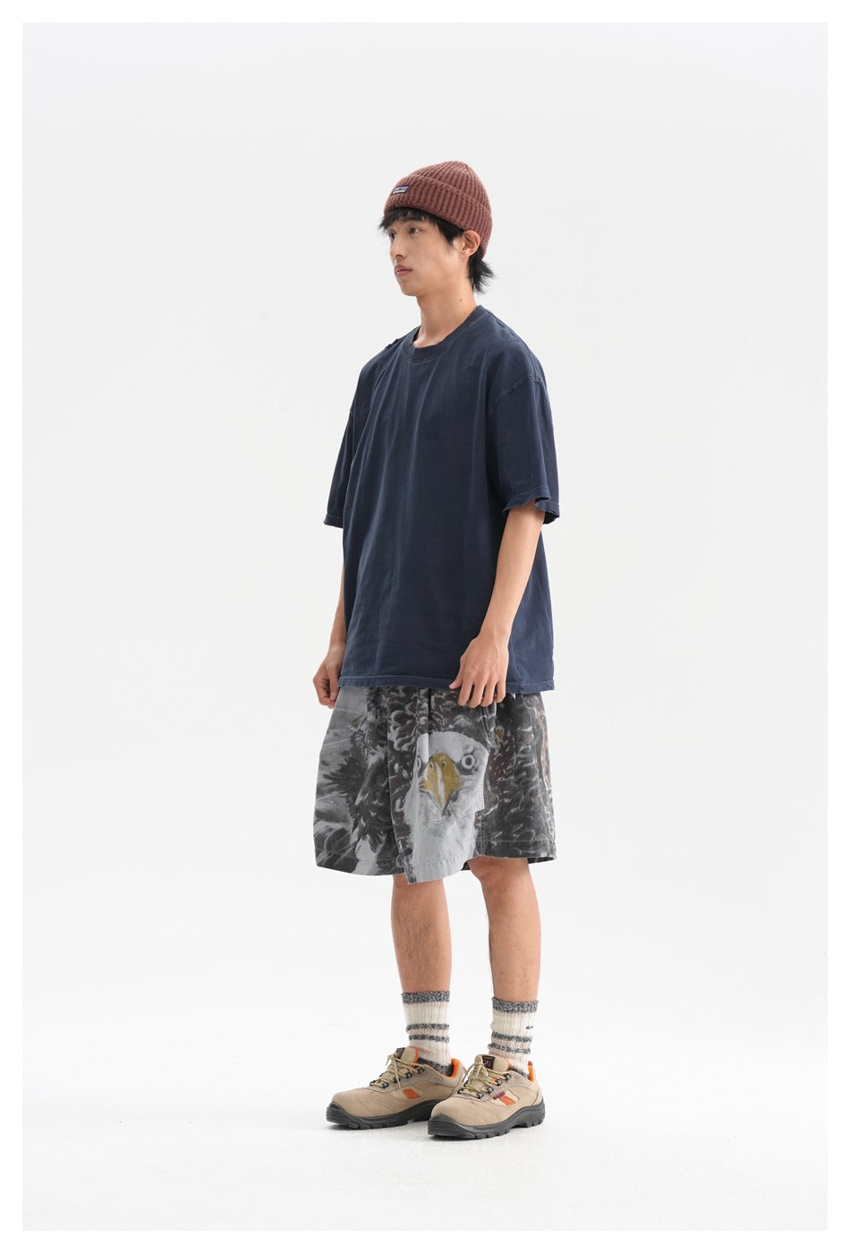 Model wearing an oversized navy T-shirt, gray shorts with a large eagle graphic, and a brown knit beanie.