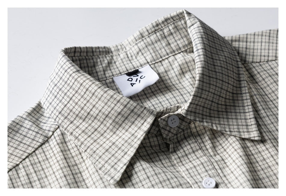 Close-up of a cream shirt with a fine black-and-gray plaid, pointed collar, white buttons, and a visible neck label.