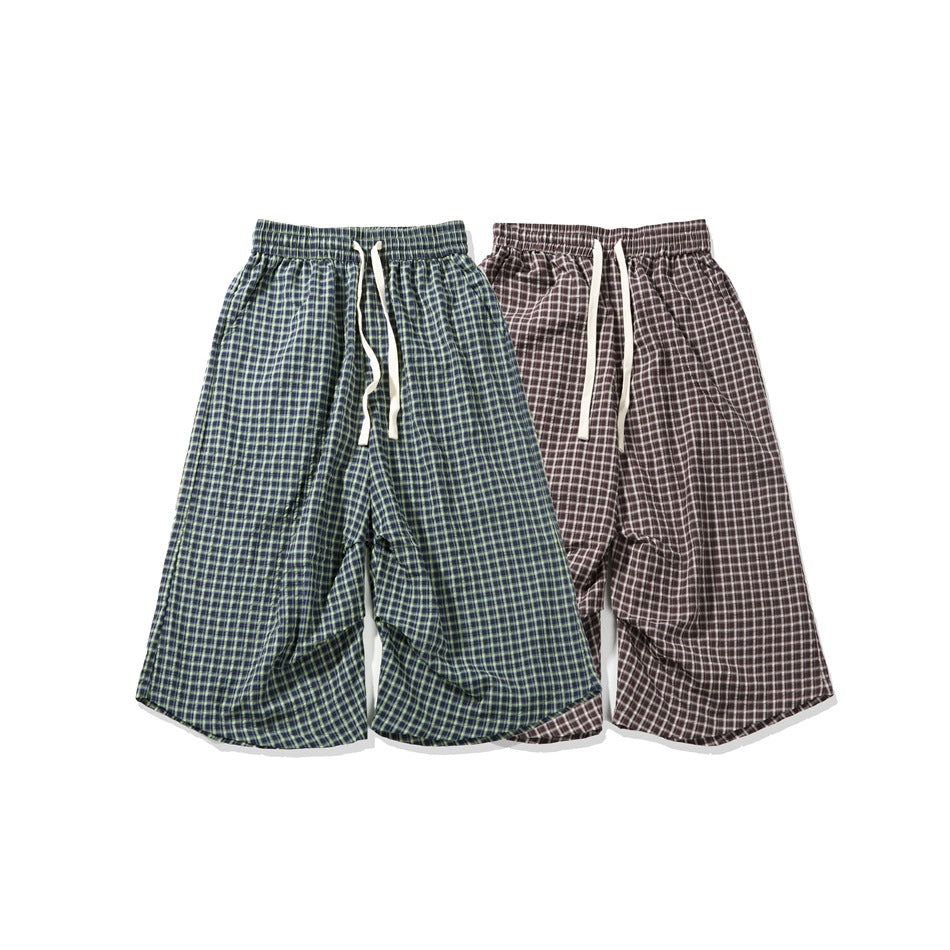 Two pairs of loose plaid shorts displayed together, one navy with green checks and one brown with white checks.
