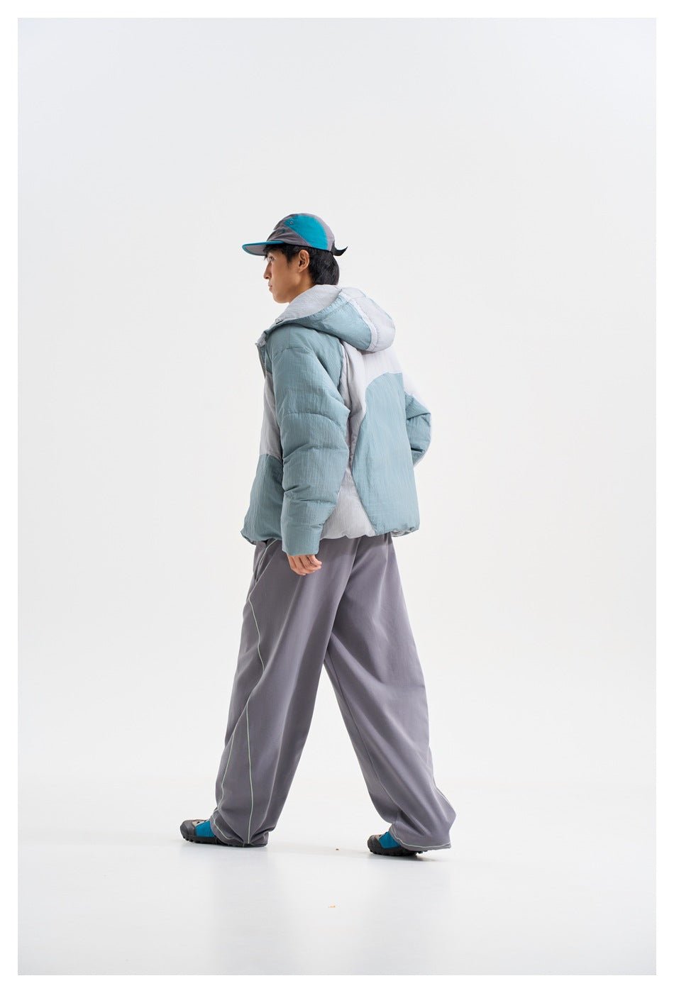 A model turns to show the back and side of a hooded puffer jacket with pale blue, gray, and white color blocking.