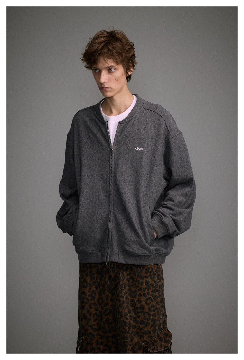 Model wearing an oversized charcoal gray zip-up jacket with a small chest logo and brown leopard-print cargo pants.