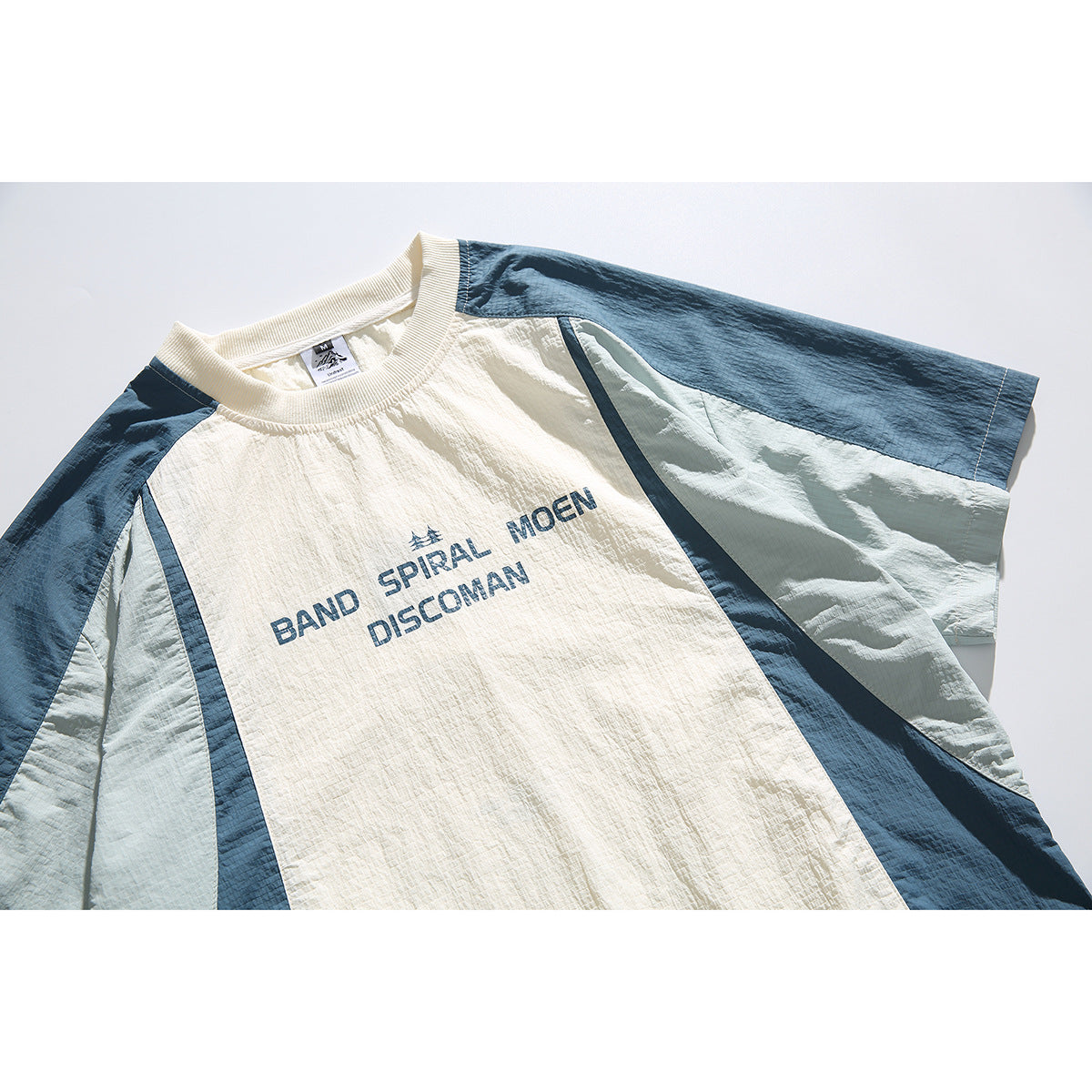 Close-up of a cream color-block short-sleeve shirt with dark blue and pale blue panels and English chest print.