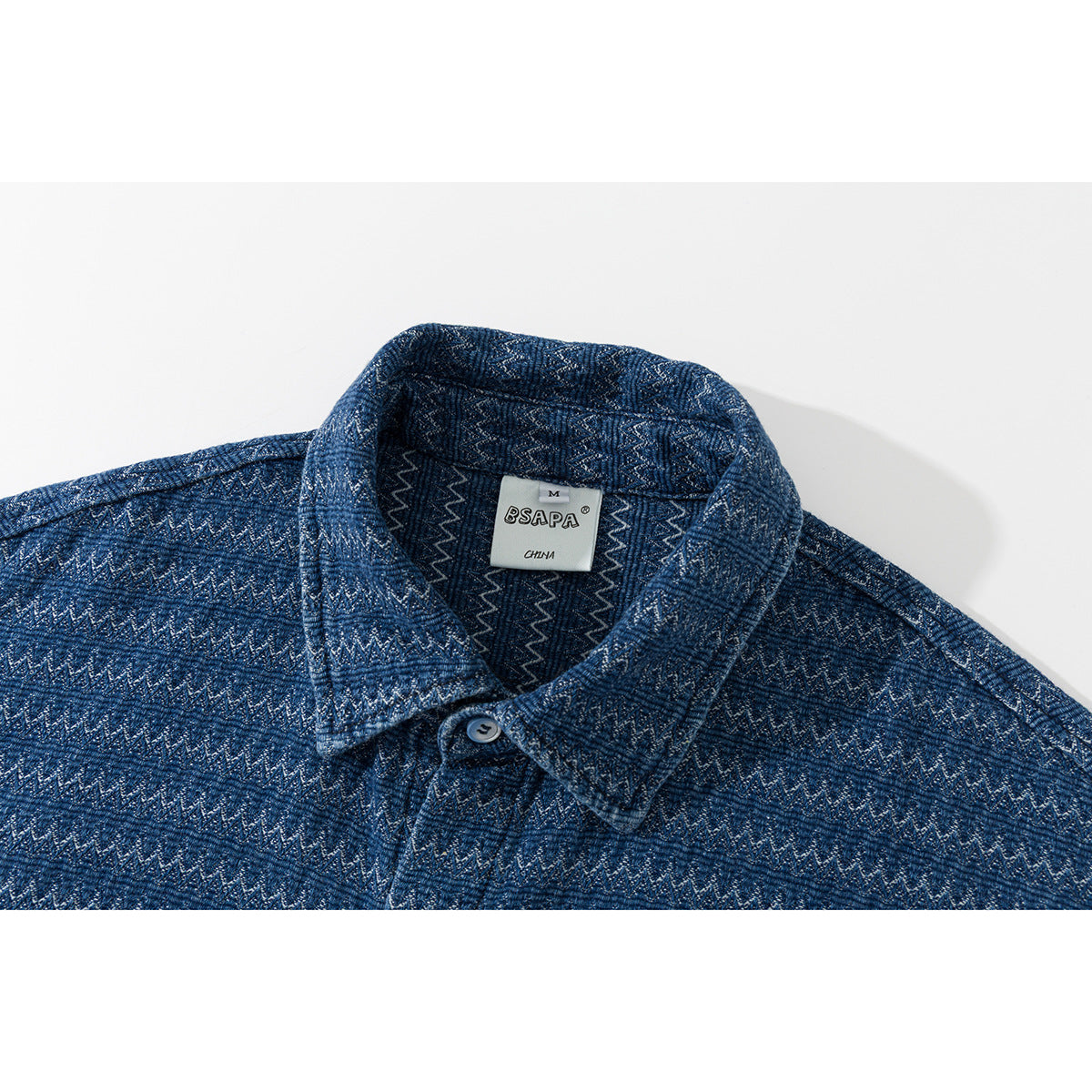 Close-up of the blue patterned shirt collar, top button, and sewn-in neck label.