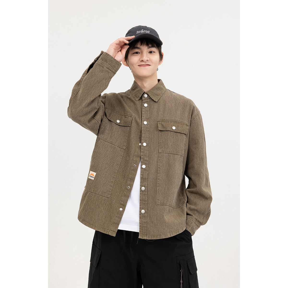 Model wearing an olive-brown button-up overshirt with flap chest pockets over a white tee and black cargo shorts.