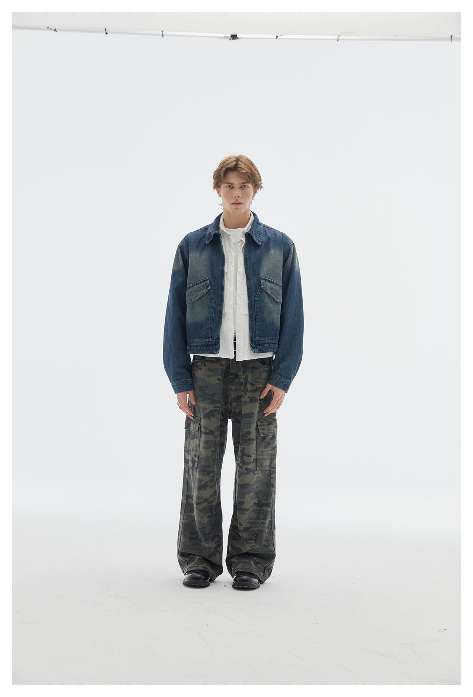 Model wearing camouflage cargo pants with a cropped denim jacket and white shirt, standing in a studio, front view