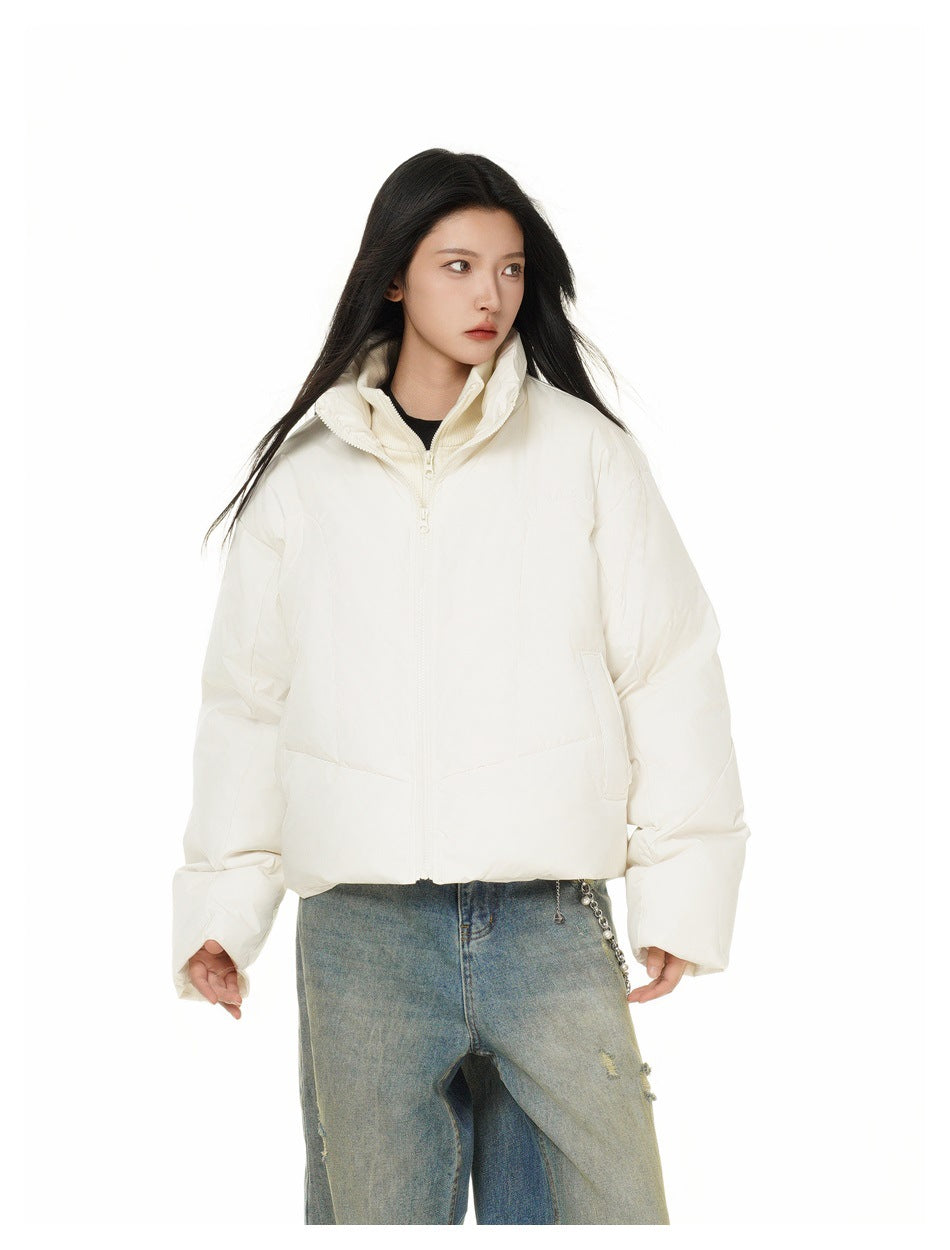 Woman wearing a cropped off-white zip-up puffer jacket with a stand collar and cream knit layer, with faded jeans
