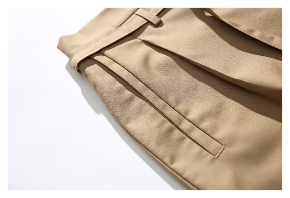 Close-up of tan trousers showing a slanted side pocket and pleated fabric.