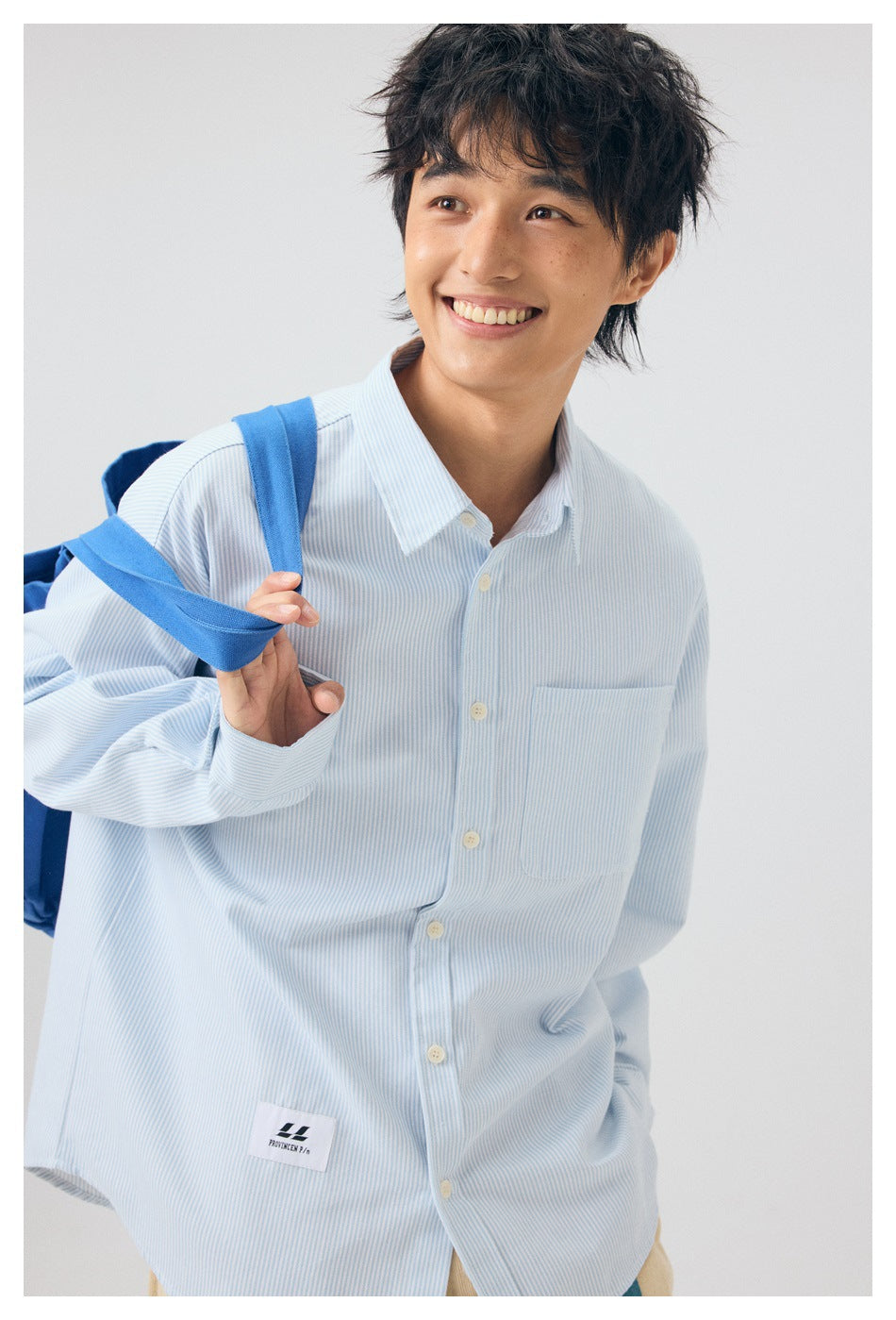 Close view of a smiling model wearing a pale blue and white pinstriped shirt with a chest pocket.